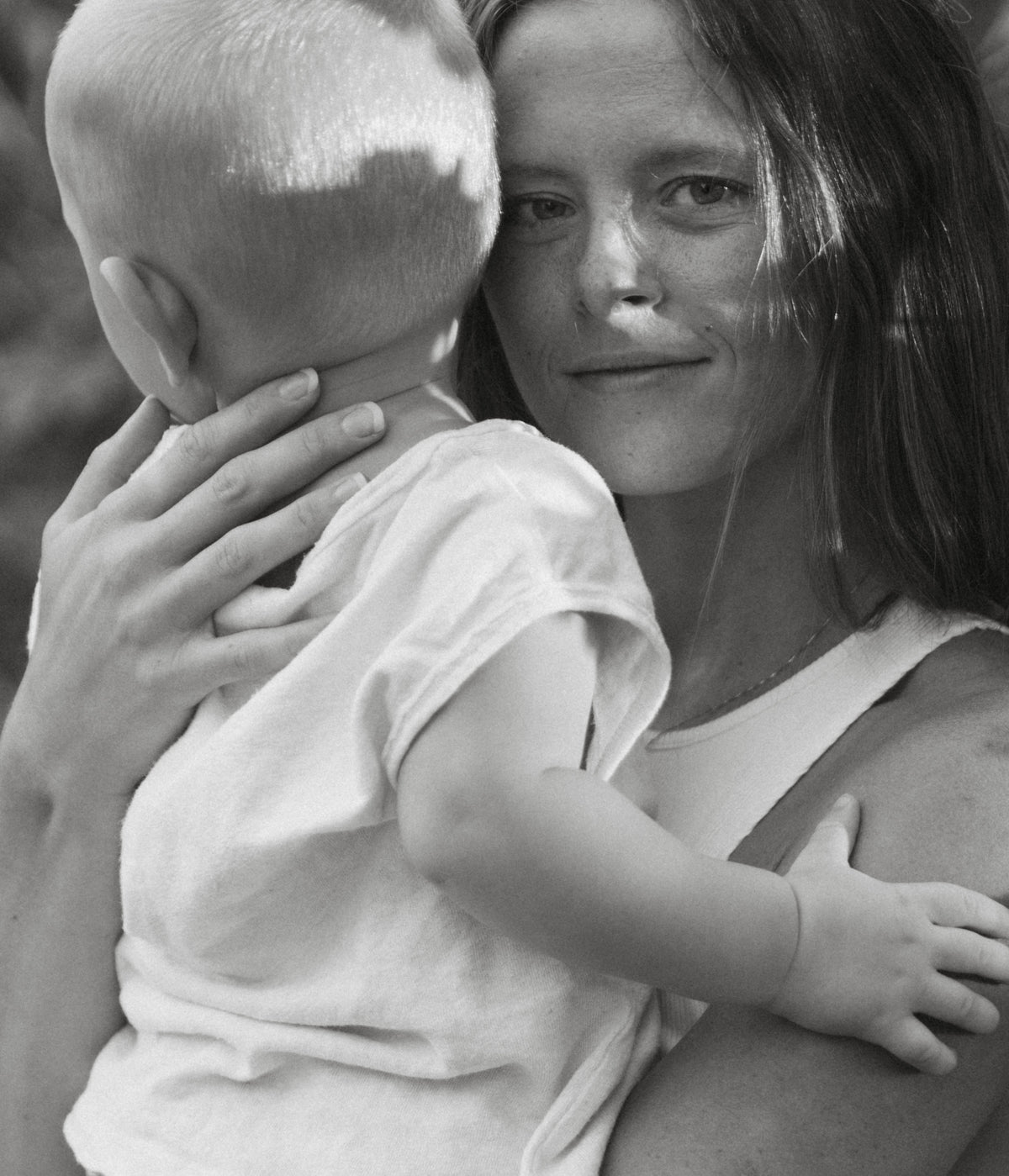 Mother holding her baby close in a black-and-white portrait, with the baby facing her and resting against her chest.