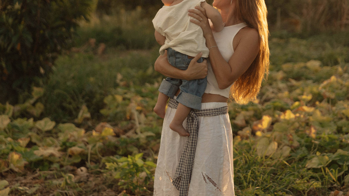 Mother holding her young child in a sunlit field during golden hour.