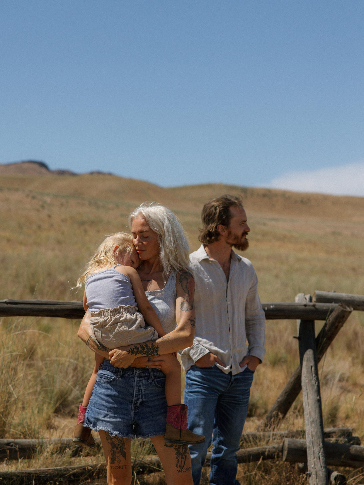 Salt Folk founders Kaelynn and Jordun with their daughter, Murphy, held close in an open grassy landscape.