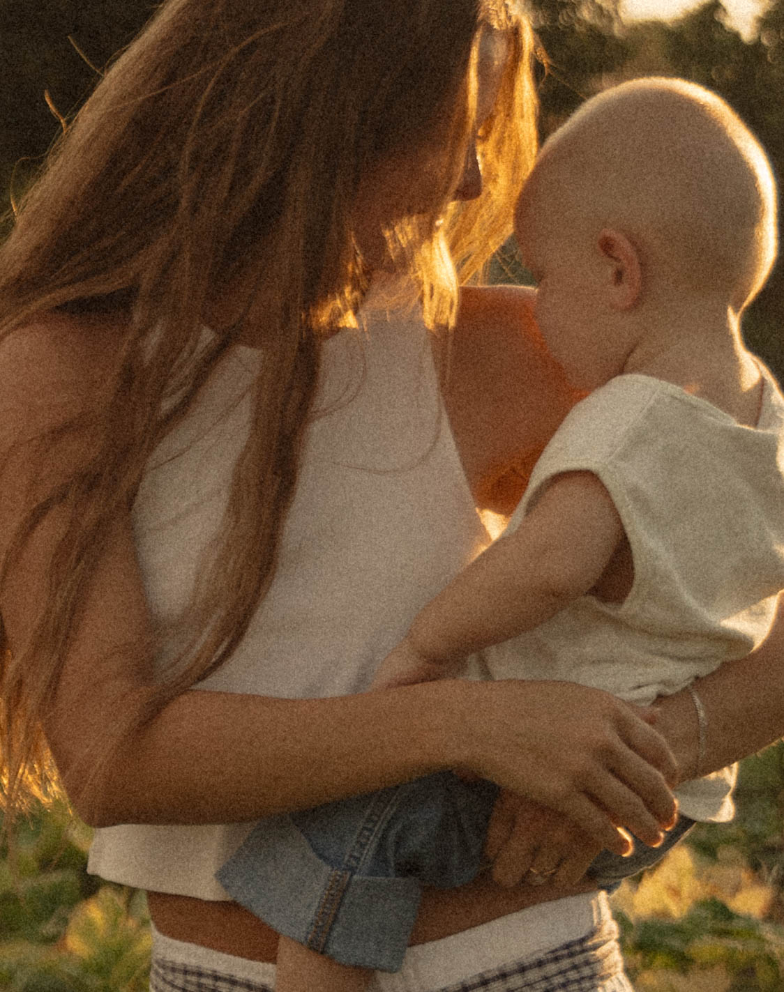 Mother holding her young child as warm golden sunlight filters through her hair.